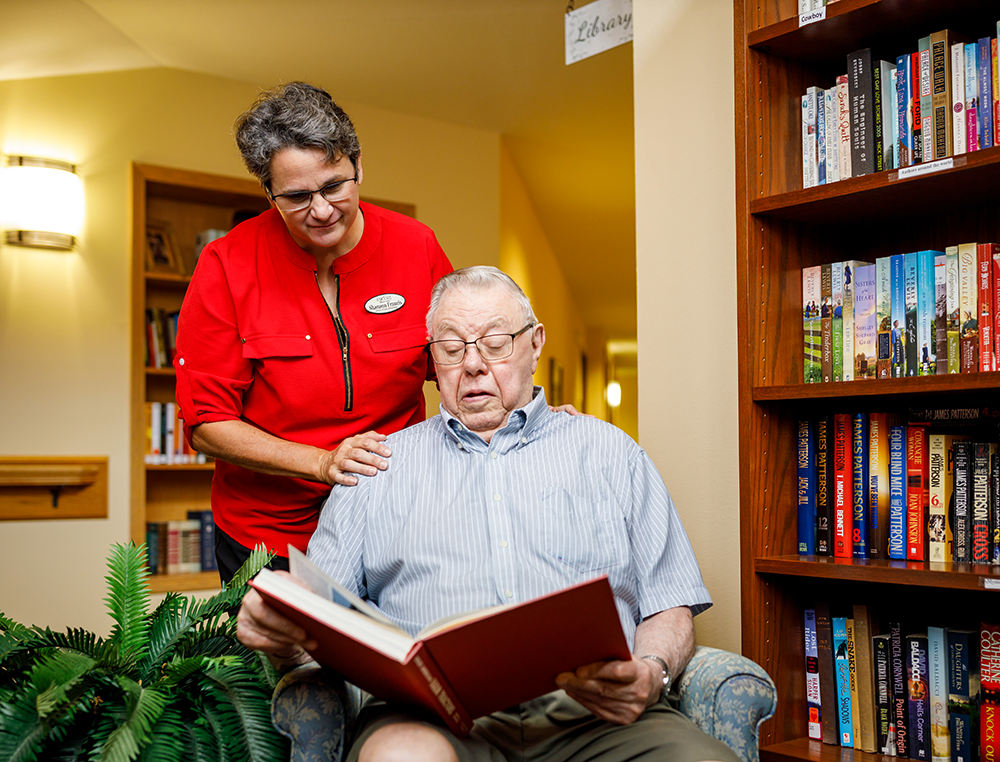 Staff member reading over the shoulder of a resident in the library