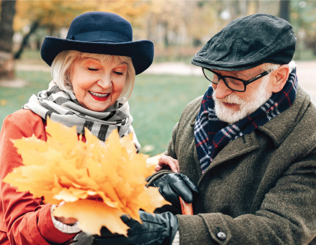 Senior woman with a bouquet of autumn leaves with her onlooking male friend.